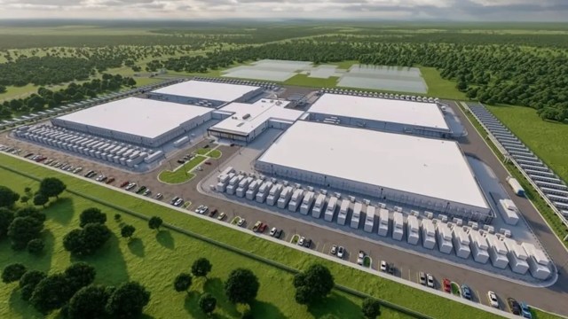 Aerial view of a large industrial facility with multiple buildings and parked vehicles in a green landscape.
