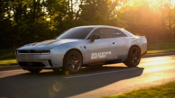 A modern electric car with "Drive" and "Solid State Battery" graphics is speeding along a tree-lined road at sunset.