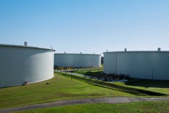 Three large, cylindrical storage tanks are situated on grass.