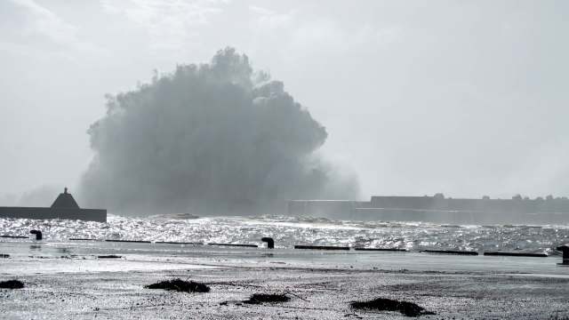 A powerful wave crashes against a breakwater.