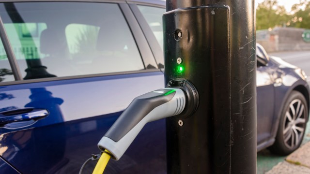 An electric vehicle charging station with a charging cable plugged in and a green indicator light illuminated.