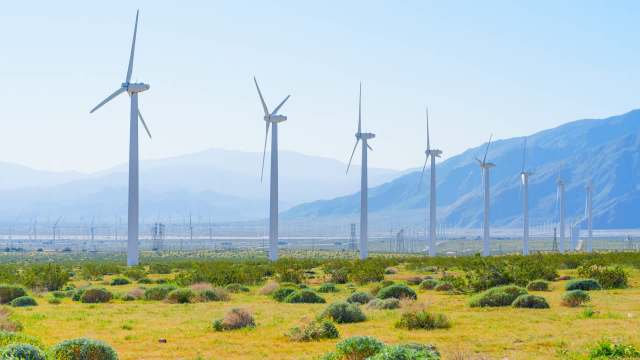 A landscape featuring numerous wind turbines with mountains and a clear blue sky in the background.