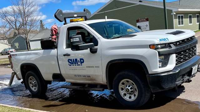 A white Chevrolet truck with a water hose attached, parked on a wet street in front of residential buildings.