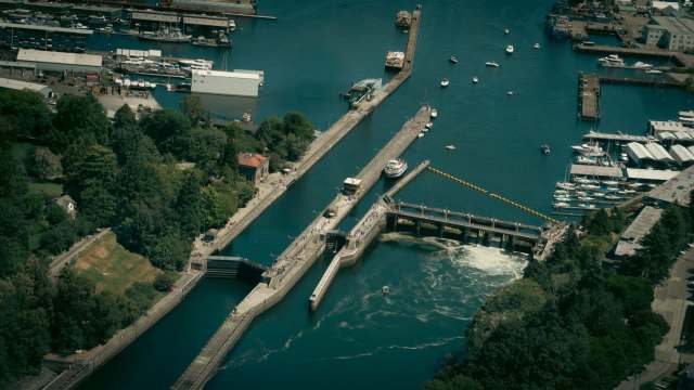 Aerial view of a marina with boats, a dam, and surrounding greenery along a waterway.