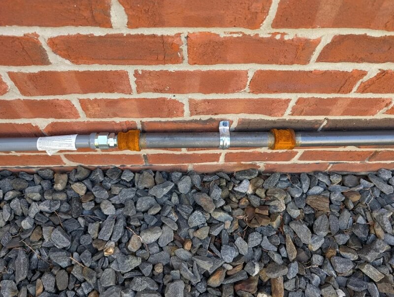 An unpainted pipe next to a masonry wall.