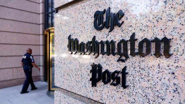 The entrance of The Washington Post building with a police officer walking past it.