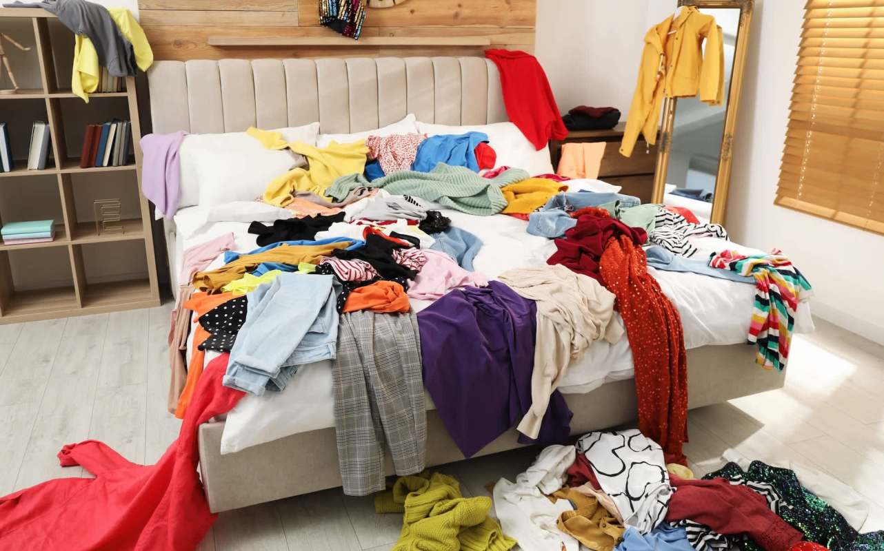 A messy bed covered in a variety of colorful clothes and garments scattered on the floor.