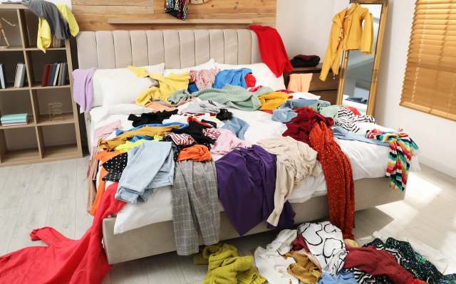 A messy bed covered in a variety of colorful clothes and garments scattered on the floor.