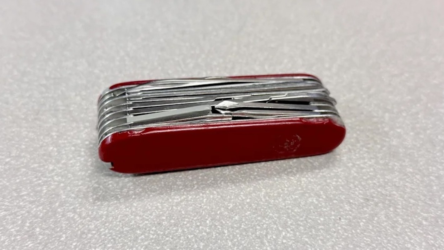 A red multi-tool with various silver metal tools folded inside it, resting on a light-colored surface.
