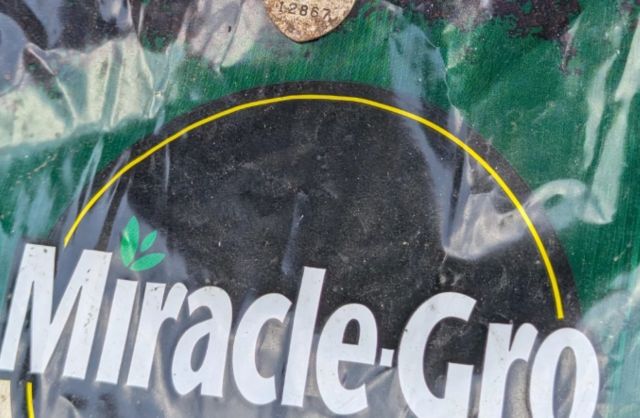 A Miracle-Gro fertilizer bag with a partially visible product label and dirt.