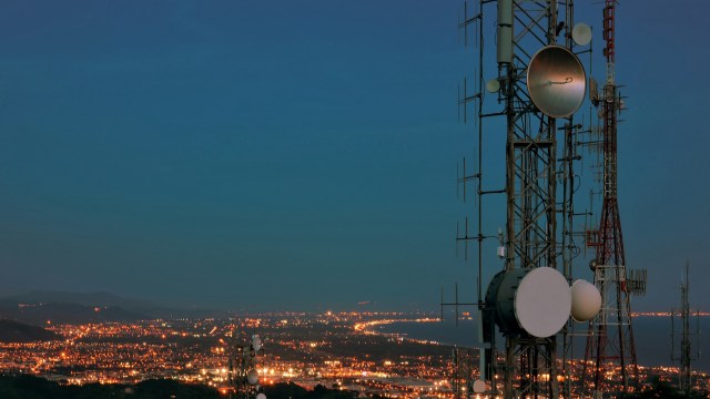 Telecommunication towers stand against a twilight sky, overlooking a city illuminated by lights.