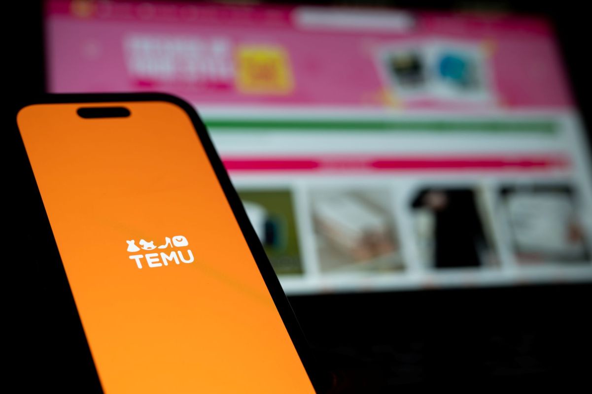 A smartphone displaying the Temu app logo with a blurred online shopping website in the background.