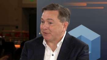 Teradata CEO Steve McMillan speaks into a microphone during an interview, wearing a dark blazer and white shirt.