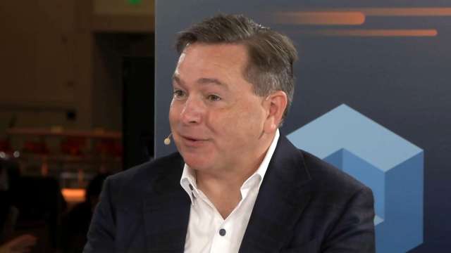 Teradata CEO Steve McMillan speaks into a microphone during an interview, wearing a dark blazer and white shirt.