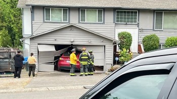 People stand near a Tesla car that's stuck in a garage.
