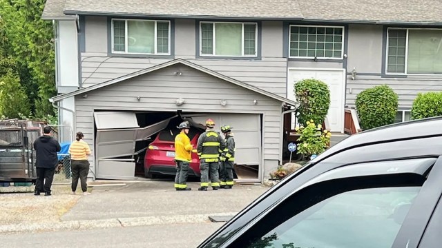 People stand near a Tesla car that's stuck in a garage.