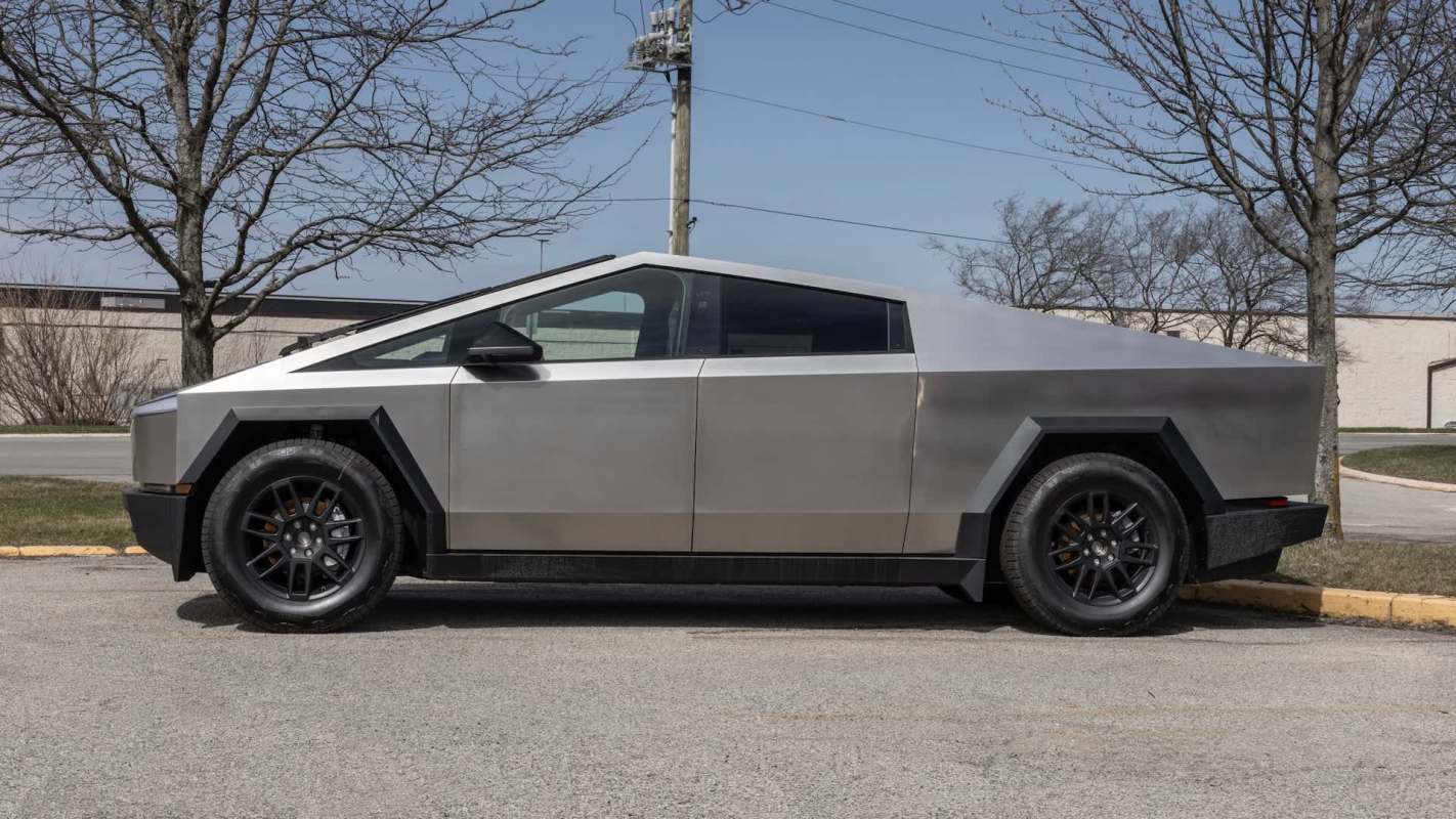 A futuristic, angular silver electric vehicle parked on a concrete surface with bare trees in the background.