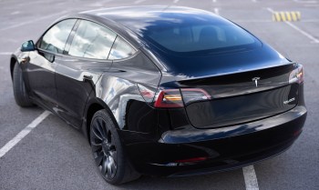 A black Tesla Model 3 in an empty parking lot.
