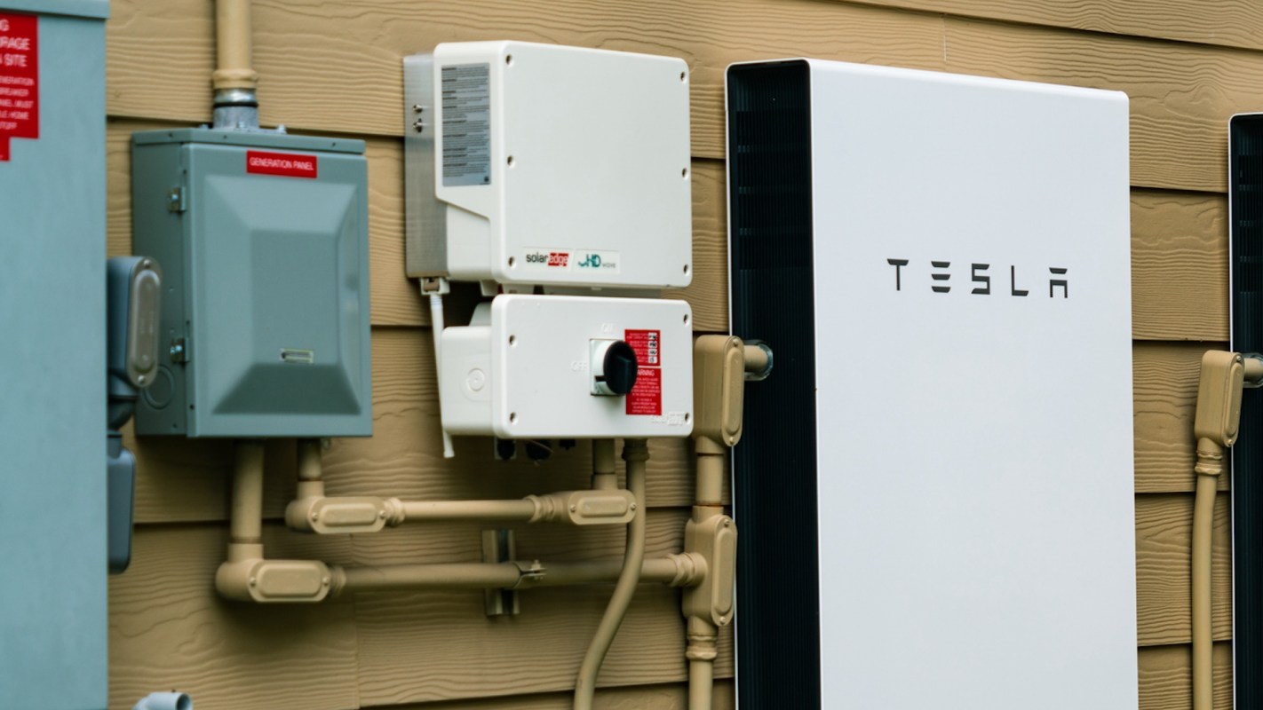 A Tesla Powerwall and solar inverters mounted on a house’s exterior wall.
