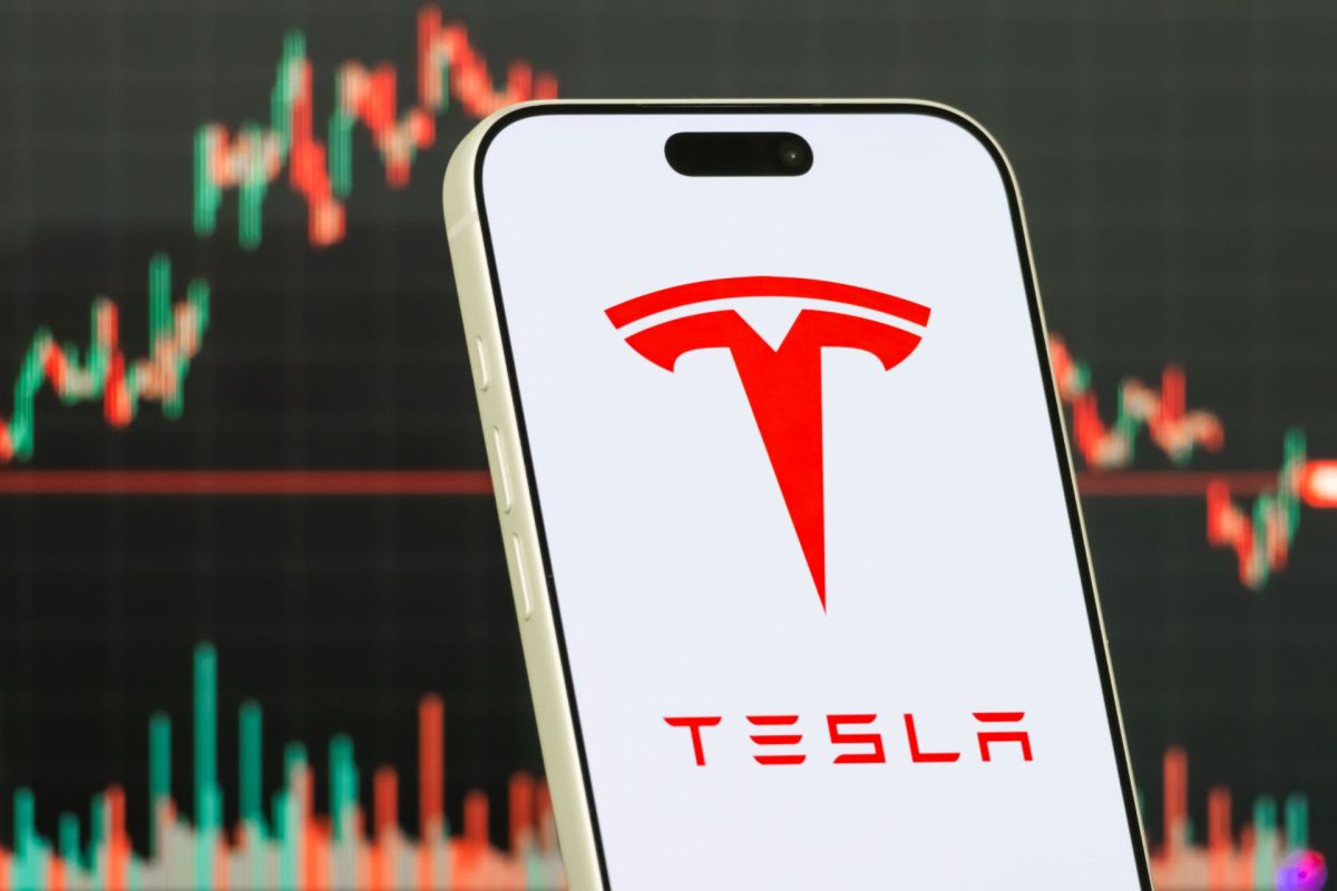 A smartphone displaying the Tesla logo with a financial chart in the background.