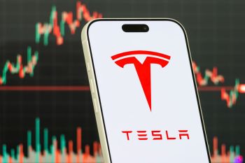 A smartphone displaying the Tesla logo with a financial chart in the background.