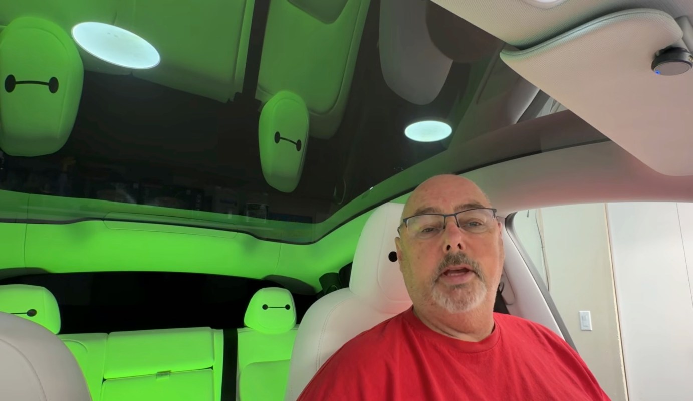 A man in a Tesla Model Y with green lighting and white stylized headrests.