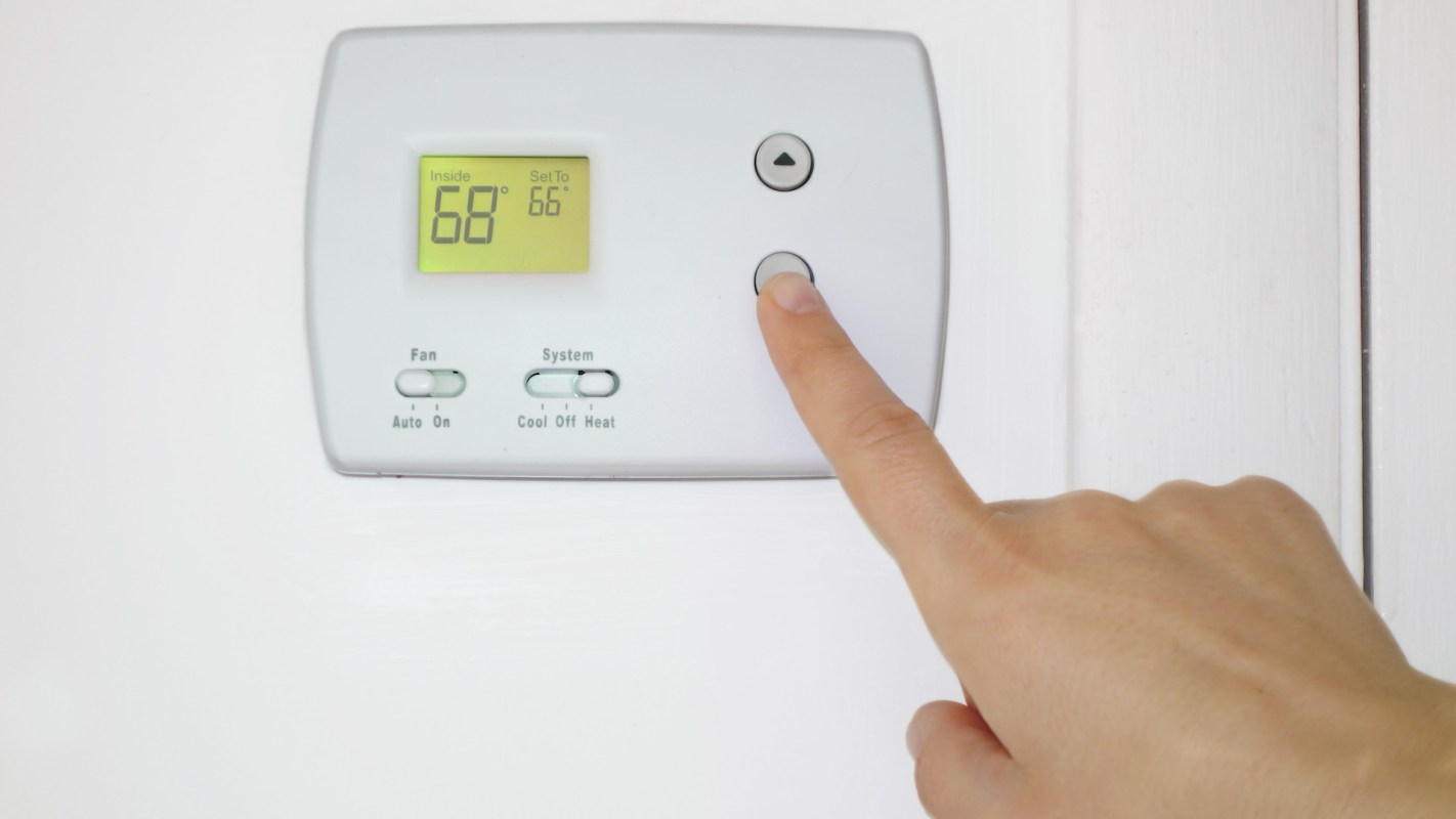 A hand adjusts a thermostat displaying an inside temperature of 68°F.