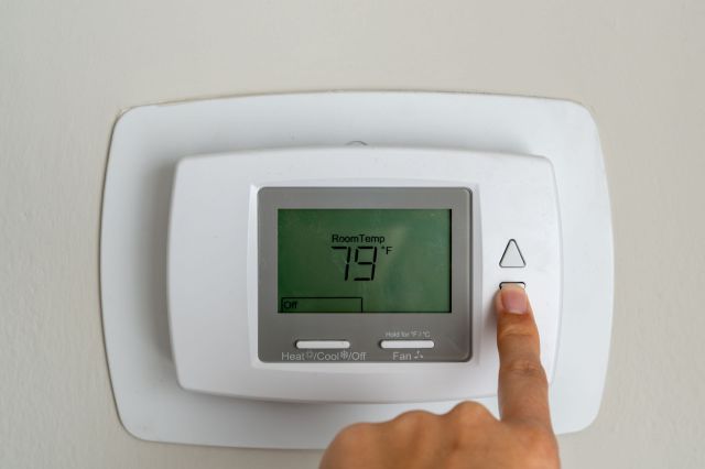 A hand turns down a thermostat's temperature.