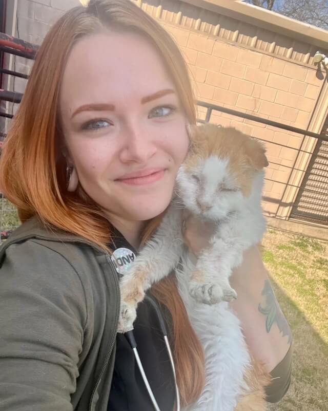 A red-haired woman posing for a selfie with an orange-and-white cat.