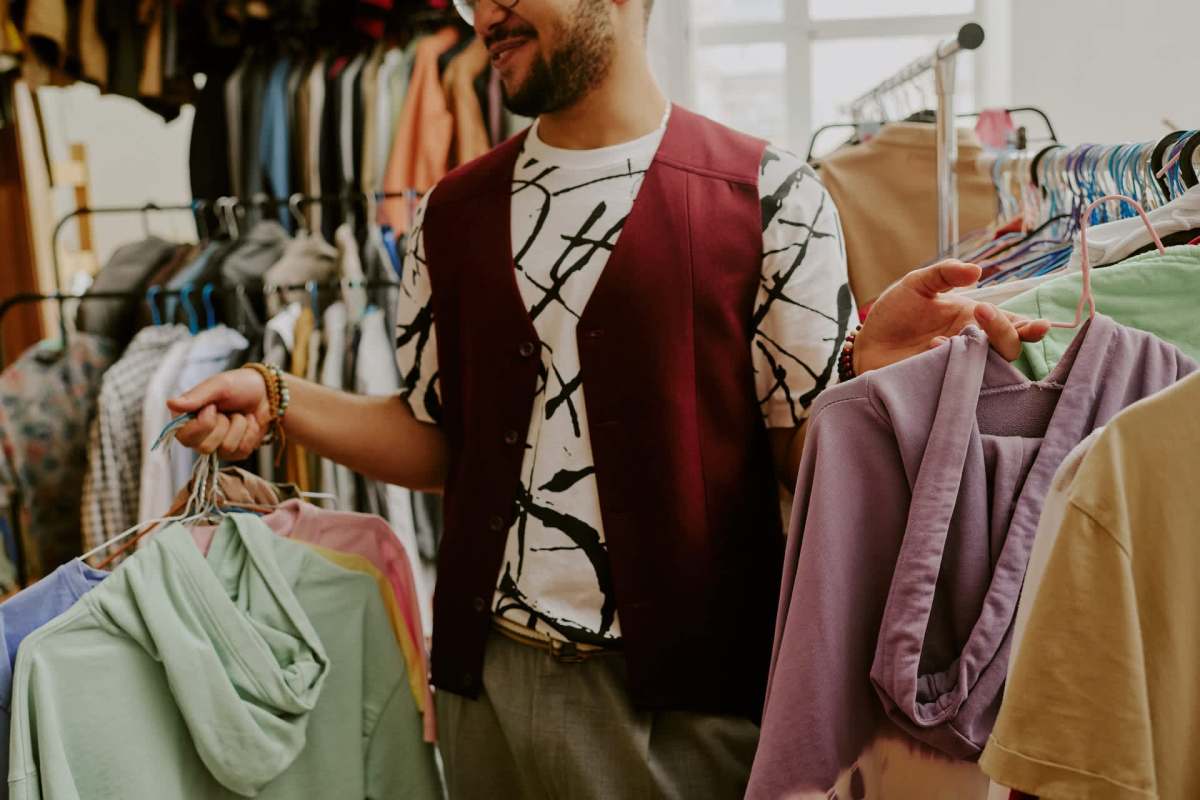 A man holds colorful clothing items while browsing a rack in a clothing store.