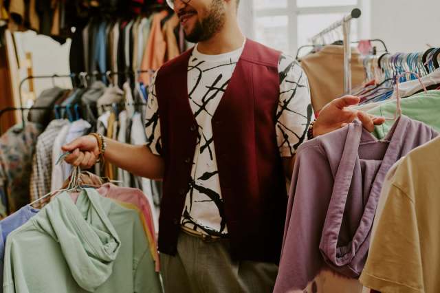 A man holds colorful clothing items while browsing a rack in a clothing store.