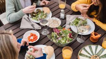 People sitting at a wooden table and enjoying salads, bread, and drinks.