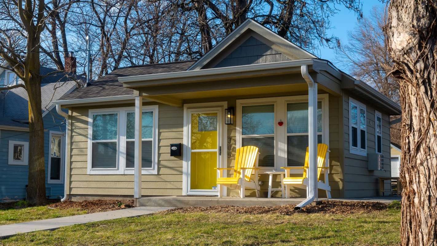 A tiny home with a yellow door and porch featuring matching yellow chairs.