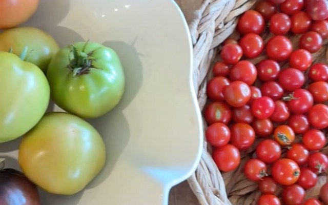 A variety of green and red tomatoes arranged in a dish and a woven basket.