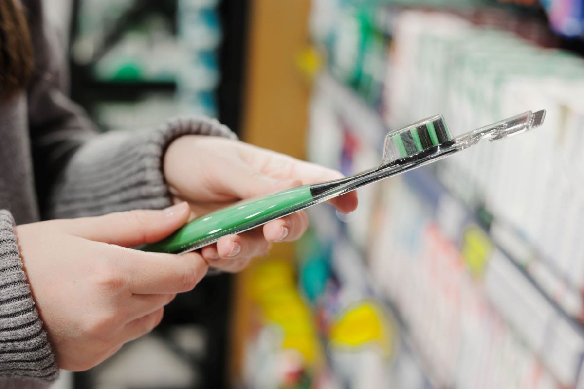 A person holds a toothbrush package while shopping in a store aisle filled with personal care items.