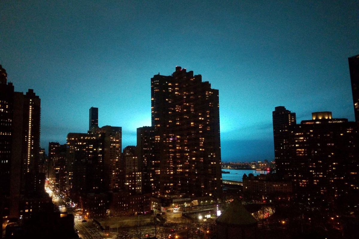 A city skyline at night, with a transformer explosion behind the buildings lighting up the ski bright blue