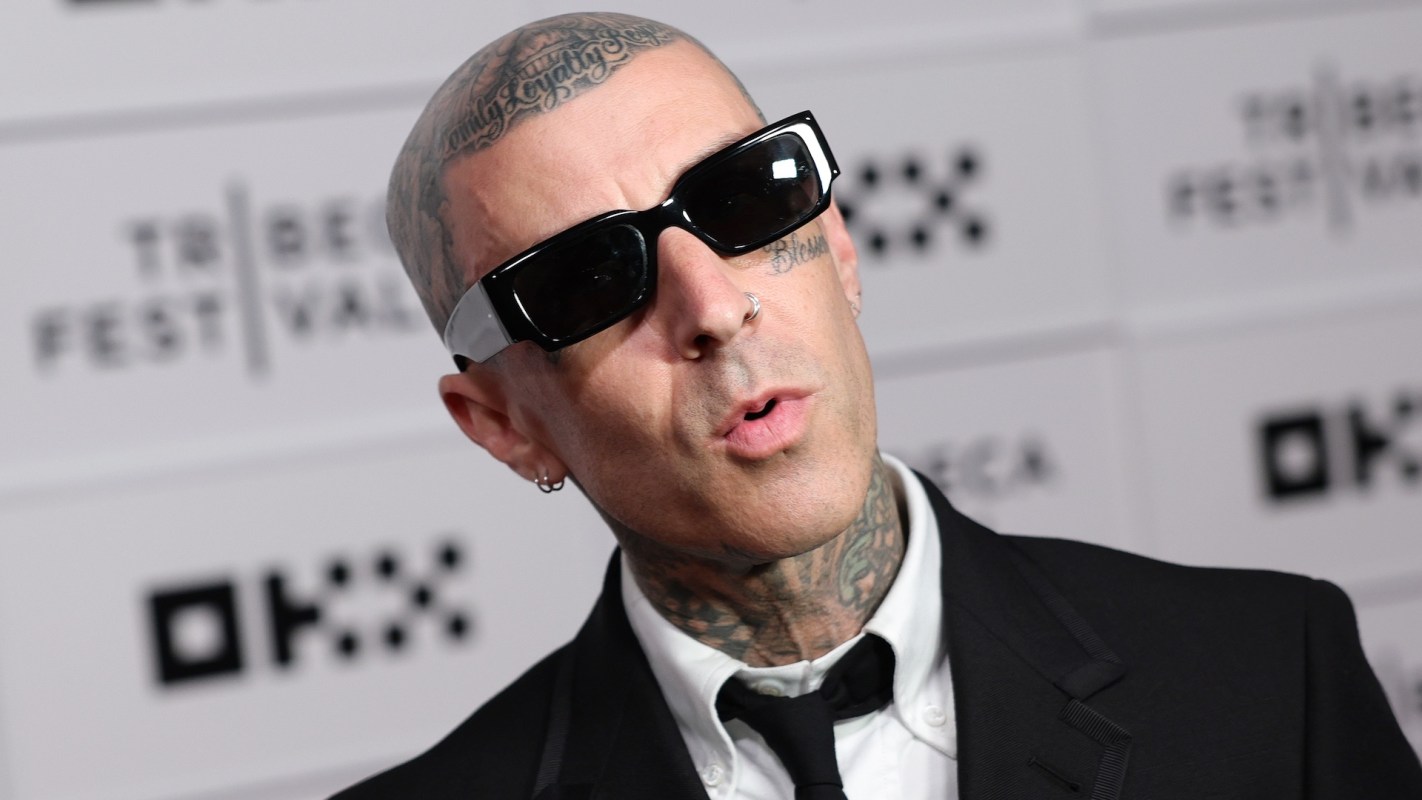 Travis Barker poses in a black suit and sunglasses at a promotional event.