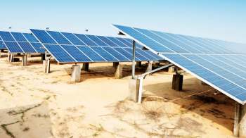 Solar panels arranged in rows on a sandy area under a clear blue sky.