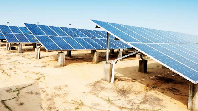 Solar panels arranged in rows on a sandy area under a clear blue sky.