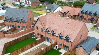 Aerial view of newly constructed brick houses with heat pumps, gardens and wooden fences in a suburban neighborhood.