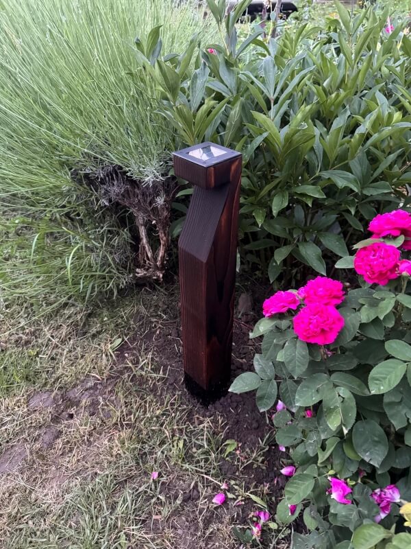 A dark wooden outdoor lamp next to a bed of plants.