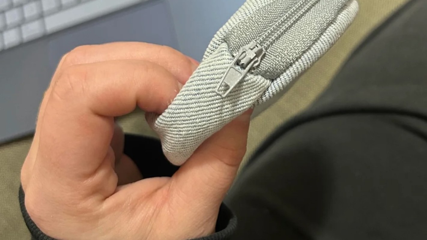 A hand holding a textured gray pouch with a zipper.