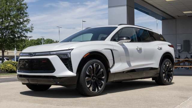 A sleek white SUV with black accents parked outside a dealership on a sunny day.