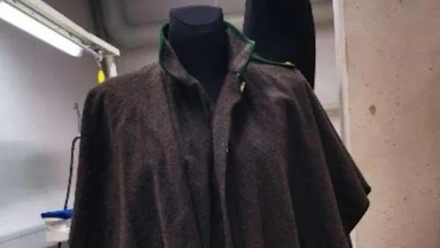 A dark, elegant cloak displayed on a mannequin in a well-lit room.
