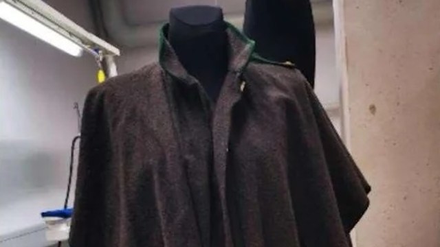 A dark, elegant cloak displayed on a mannequin in a well-lit room.