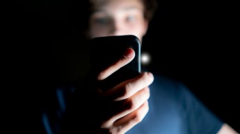 A person is holding a smartphone, illuminated by its screen in a dark environment.