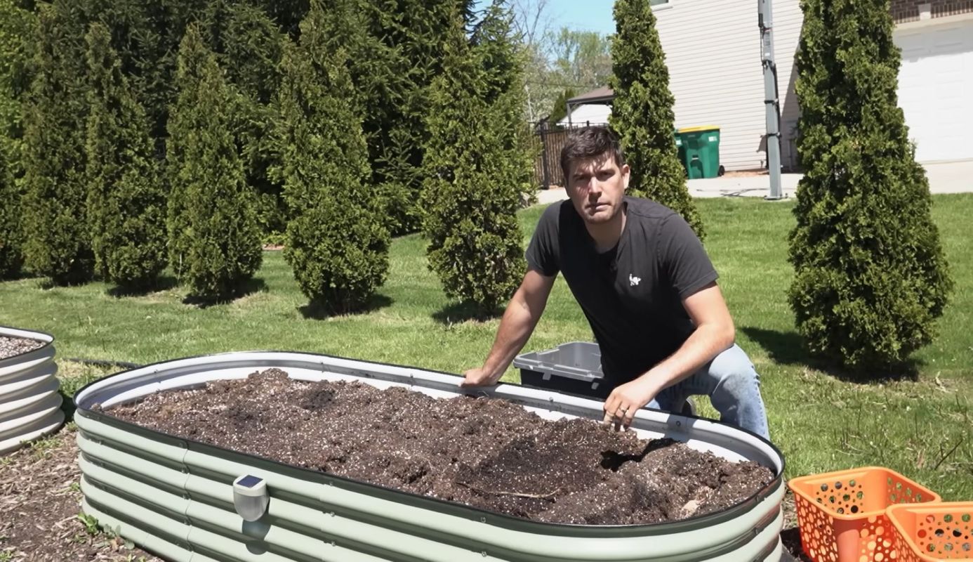 A man leans over a soil-filled raised garden bed.