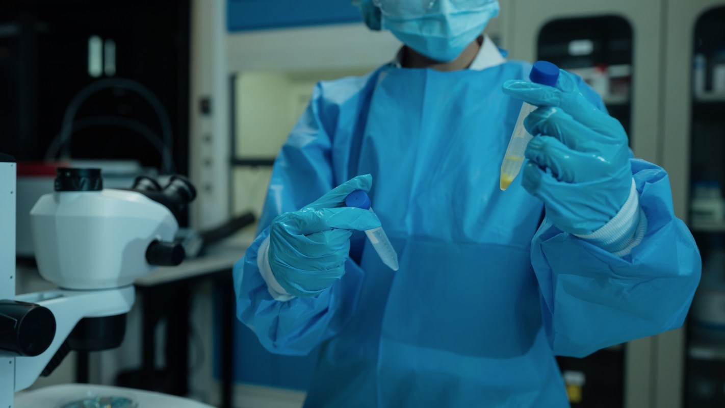 A scientist in blue protective gear holding test tubes.