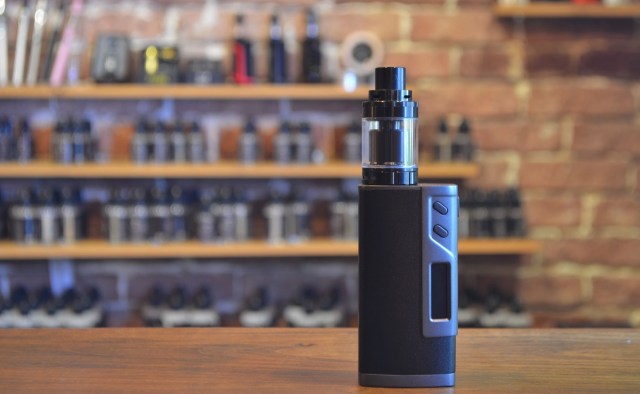 A black vape on a wooden table in front a blurred background.