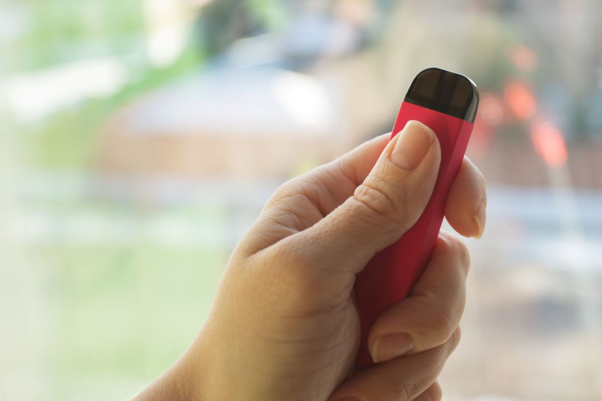 A hand holding a red and black vape.